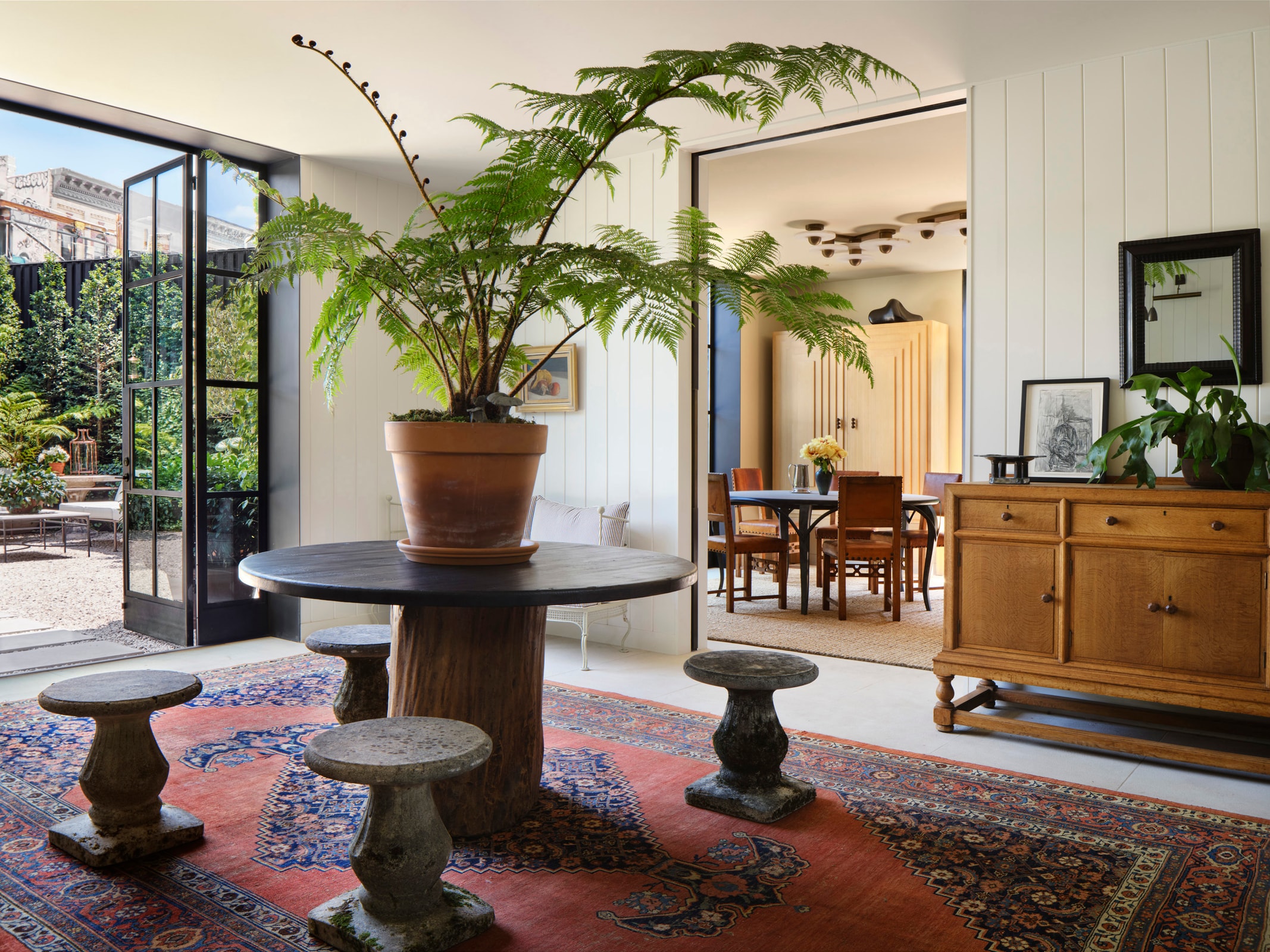 Entryway table topped with large potted plants and four short stone chairs, with view into Damien Harrison's office